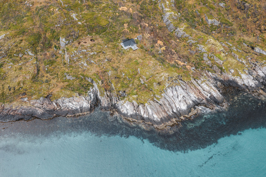 Aerial view of a solitary house perched on the rugged rocky cliffs of Senja island overlooking the clear turquoise waters of the Norwegian Sea in Senja Troms Norway.