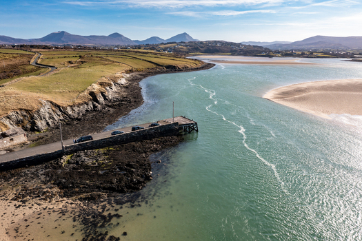 Aerial view of Ballyness Bay featuring a stone pier extending into the turquoise waters with rolling green hills and sandy tidal flats in Ballyness County Donegal Ireland. Aerial view of Ballyness Bay featuring a stone pier extending into the turquoise waters with rolling green hills and sandy tidal flats in Ballyness County Donegal Ireland.