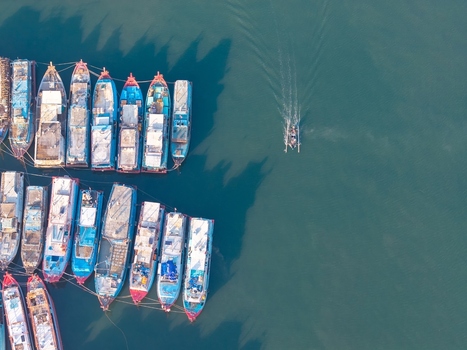 Aerial view of fishing boats moored in the harbor with a small boat navigating the calm blue water in Probolinggo East Java Indonesia.