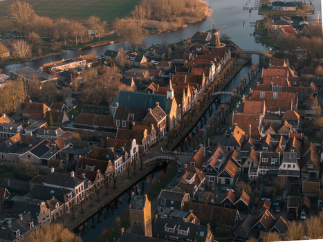 Aerial view of the historic town of Sloten with its winding canals traditional gabled houses and a classic windmill under warm golden hour light Sloten Friesland Netherlands. Aerial view of the historic town of Sloten with its winding canals traditional gabled houses and a classic windmill under warm golden hour light Sloten Friesland Netherlands.