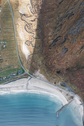 Aerial view of the rugged coastline of Senja island featuring a winding stream steep mountain slopes a sandy beach and a coastal road in Senja Troms Norway.