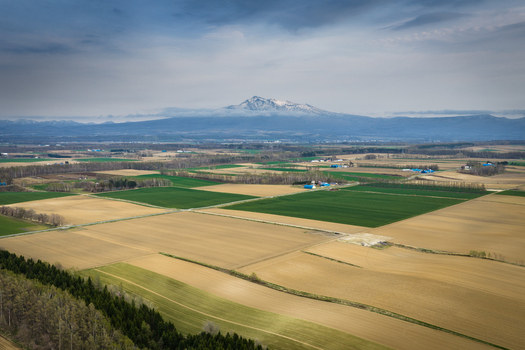 Aerial view of the agricultural landscape near Lake Kussharo with patchwork fields distant snow capped mountains and a cloudy sky in Teshikaga Hokkaido Japan. Aerial view of the agricultural landscape near Lake Kussharo with patchwork fields distant snow capped mountains and a cloudy sky in Teshikaga Hokkaido Japan.