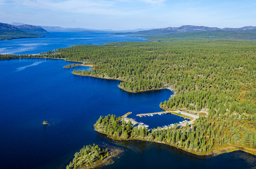 Aerial view of Lake Femund featuring a small marina with docked boats surrounded by dense pine forests and deep blue water in Norway. Aerial view of Lake Femund featuring a small marina with docked boats surrounded by dense pine forests and deep blue water in Norway.