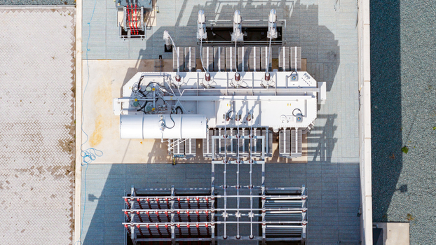Aerial view of an electrical substation transformer with cooling fins and high voltage equipment on a paved site in Espel Flevoland Netherlands. Aerial view of an electrical substation transformer with cooling fins and high voltage equipment on a paved site in Espel Flevoland Netherlands.