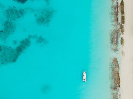 Aerial view of a lone boat contrasts against the turquoise sea meeting the white sandy shore Vashafaru Island Thiladhummathi Atoll Maldives. Aerial view of a lone boat contrasts against the turquoise sea meeting the white sandy shore Vashafaru Island Thiladhummathi Atoll Maldives.