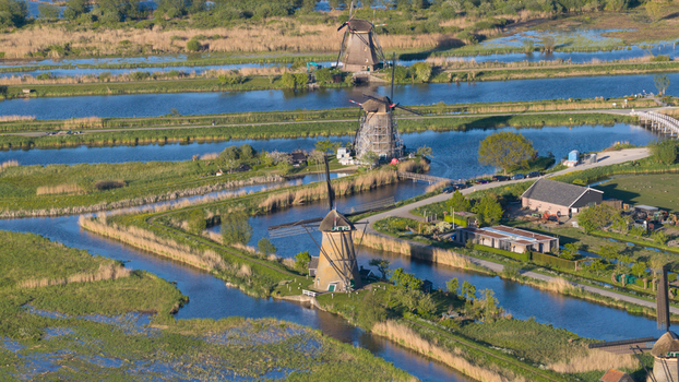 Aerial view of historic windmills standing along blue canals surrounded by lush green fields and reeds Kinderdijk South Holland Netherlands. Aerial view of historic windmills standing along blue canals surrounded by lush green fields and reeds Kinderdijk South Holland Netherlands.