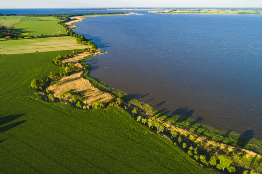 Aerial view of the coastline of Lake Vanern with lush green fields and trees in Vanersnas Vastra Gotalands lan Sweden. Aerial view of the coastline of Lake Vanern with lush green fields and trees in Vanersnas Vastra Gotalands lan Sweden.