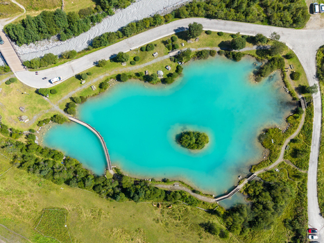 Aerial view of the turquoise Sulden lake with a small island wooden footbridges surrounding green meadows and mountain paths in Sulden Trentino Alto Adige Italy. Aerial view of the turquoise Sulden lake with a small island wooden footbridges surrounding green meadows and mountain paths in Sulden Trentino Alto Adige Italy.