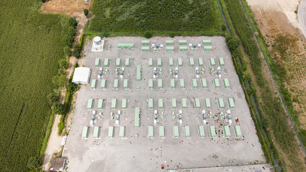 Aerial view of a battery energy storage system with rows of green containers and power grid infrastructure surrounded by agricultural fields in Tavazzano con Villavesco Lombardy Italy.