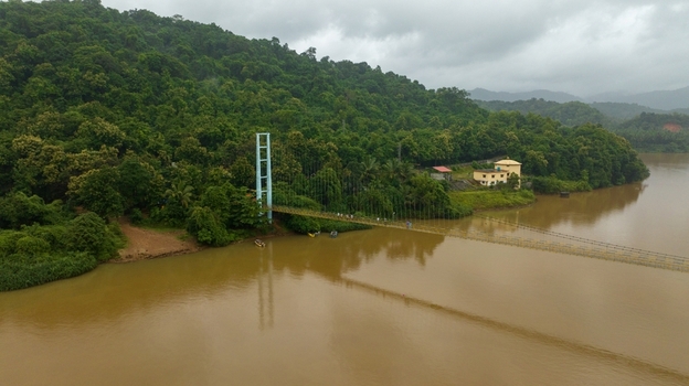 Aerial view of the suspension bridge spanning the river surrounded by lush green hills and dense forest under a cloudy sky in Honnavar Karnataka India.