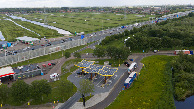 Oostzaan Netherlands 09 June 2026 Aerial view of the Fastned Charging Station featuring distinctive solar panel roofs situated adjacent to a busy highway with surrounding green fields.