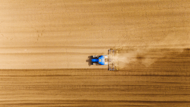 Aerial view of a blue tractor cutting through the vast dry land kicking up dust in its wake Sremska Mitrovica Vojvodina Serbia. Aerial view of a blue tractor cutting through the vast dry land kicking up dust in its wake Sremska Mitrovica Vojvodina Serbia.