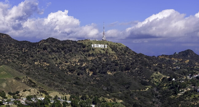 Aerial view of the iconic Hollywood sign situated on the slopes of Mount Lee surrounded by rugged hills and blue sky with scattered clouds. Hollywood California United States. Aerial view of the iconic Hollywood sign situated on the slopes of Mount Lee surrounded by rugged hills and blue sky with scattered clouds. Hollywood California United States.