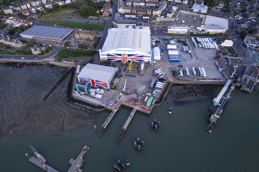 Aerial view of Wight Shipyard Co. featuring large industrial buildings with Union Jack motifs shipyard facilities docks and boats along the waterfront in Cowes England United Kingdom.