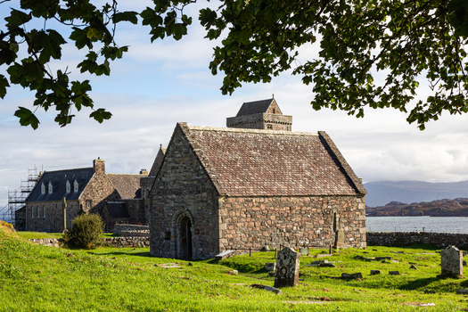 View of Iona Abbey and Nunnery with historic stone buildings and ancient graveyard overlooking the sea under a bright sky Isle of Iona Scotland United Kingdom. View of Iona Abbey and Nunnery with historic stone buildings and ancient graveyard overlooking the sea under a bright sky Isle of Iona Scotland United Kingdom.