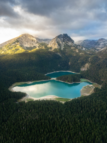 Aerial view of Crno Jezero surrounded by dense pine forests and dramatic mountain peaks under a cloudy sky in Zabljak Zabljak Municipality Montenegro. Aerial view of Crno Jezero surrounded by dense pine forests and dramatic mountain peaks under a cloudy sky in Zabljak Zabljak Municipality Montenegro.