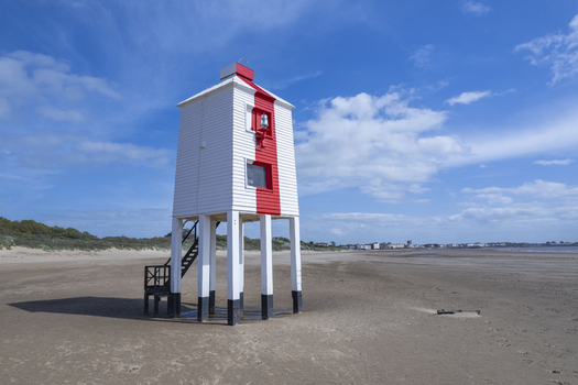 Aerial view of the historic Burnham on Sea Low Lighthouse standing on wooden stilts on the sandy beach under a clear blue sky in Burnham on Sea England United Kingdom.