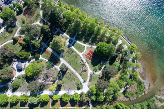 Aerial view of Parc de l Independance with vibrant flower beds winding paths and lush green trees along the shores of Lake Geneva in Morges Vaud Switzerland. Aerial view of Parc de l Independance with vibrant flower beds winding paths and lush green trees along the shores of Lake Geneva in Morges Vaud Switzerland.