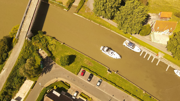Aerial view of boats moored in the canal near a bridge and a parking area surrounded by lush greenery in Saint Omer Hauts de France France. Aerial view of boats moored in the canal near a bridge and a parking area surrounded by lush greenery in Saint Omer Hauts de France France.