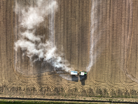 Aerial view of a tractor working in a tilled agricultural field emitting a plume of white smoke or dust in Borgo d Ale Piedmont Italy.