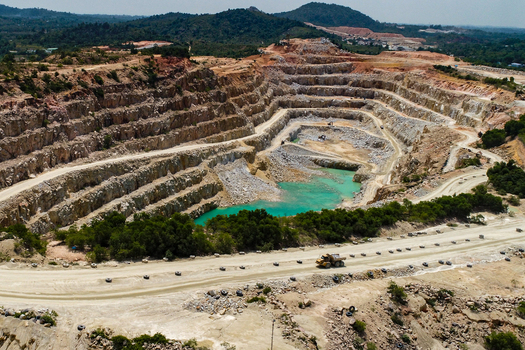 Aerial view of a gravel and sand mine featuring terraced walls a turquoise water pool and a dump truck on a dirt road in Karimun Kepulauan Riau Indonesia.