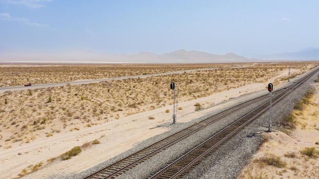 Aerial view of a railroad track stretching through the arid desert landscape with distant mountains signal lights and a nearby road with a car in the United States.