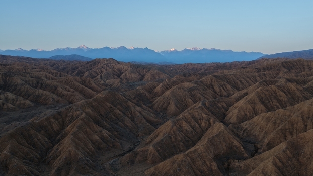 Aerial view of the rugged arid landscape of the Issyk Kul area featuring deep valleys and sharp ridges with snow capped mountains in the distance in Issyk Kul Region Kyrgyzstan. Aerial view of the rugged arid landscape of the Issyk Kul area featuring deep valleys and sharp ridges with snow capped mountains in the distance in Issyk Kul Region Kyrgyzstan.