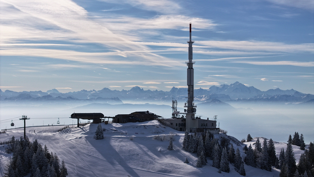 Aerial view of the Mont Rond telecommunications tower standing tall amidst a snowy landscape with a backdrop of hazy distant mountains Gex Auvergne Rhône Alpes France. Aerial view of the Mont Rond telecommunications tower standing tall amidst a snowy landscape with a backdrop of hazy distant mountains Gex Auvergne Rhône Alpes France.