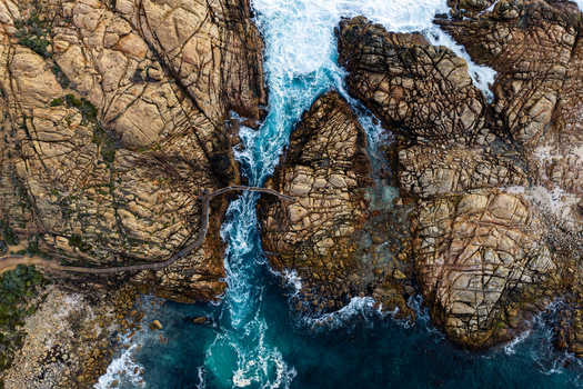Aerial view of the wooden Canal Rocks Bridge spanning rugged rock formations with turquoise ocean waves crashing below in Yallingup Western Australia Australia.