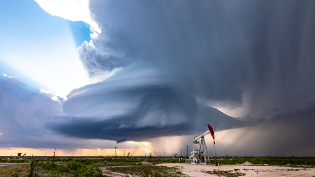 View of a dramatic supercell storm cloud looming over an oil pump jack in a vast field in Oklahoma City Oklahoma United States.