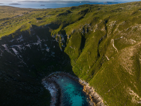 Aerial view of Torndirrup featuring dramatic rugged cliffs lush green vegetation and a secluded turquoise cove with rocky shoreline in Torndirrup Western Australia Australia. Aerial view of Torndirrup featuring dramatic rugged cliffs lush green vegetation and a secluded turquoise cove with rocky shoreline in Torndirrup Western Australia Australia.