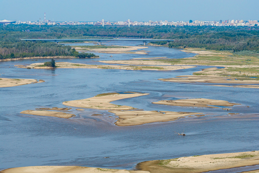 Aerial view of the Vistula river in Poland showing low water levels with extensive exposed sandbanks and a distant bridge under a clear sky.
