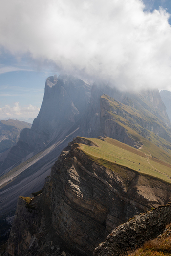 View of the Dolomites featuring jagged mountain peaks and steep grassy ridges under thick white clouds in Rocca Pietore Veneto Italy. View of the Dolomites featuring jagged mountain peaks and steep grassy ridges under thick white clouds in Rocca Pietore Veneto Italy.