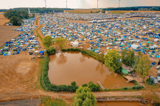 Herzogenaurach Germany 22 July 2022 Aerial view of the Open Beatz Festival campsite featuring thousands of colorful tents a small pond and wind turbines under a hazy sky. Herzogenaurach Germany 22 July 2022 Aerial view of the Open Beatz Festival campsite featuring thousands of colorful tents a small pond and wind turbines under a hazy sky.