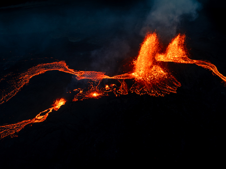 Aerial view of a volcanic eruption at night with glowing lava fountains and molten rivers flowing across the dark volcanic landscape in Iceland. Aerial view of a volcanic eruption at night with glowing lava fountains and molten rivers flowing across the dark volcanic landscape in Iceland.