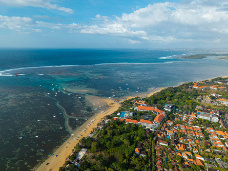 Aerial view of the coastline featuring a sandy beach turquoise waters coral reefs and a resort area in Kecamatan Denpasar Selatan Bali Indonesia.