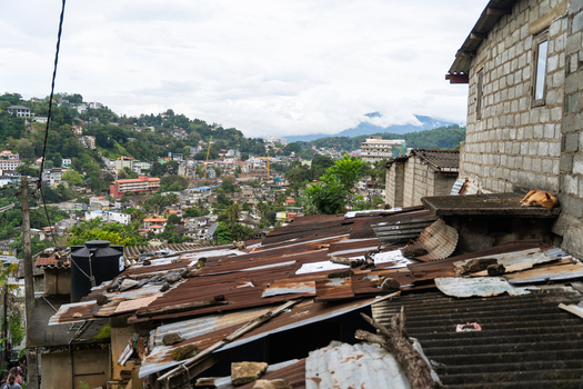 View of the urban landscape with rusty corrugated metal roofs and concrete buildings overlooking the lush green hills under a cloudy sky in Kandy Central Province Sri Lanka. View of the urban landscape with rusty corrugated metal roofs and concrete buildings overlooking the lush green hills under a cloudy sky in Kandy Central Province Sri Lanka.