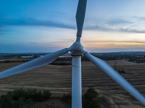 Aerial view of a wind turbine above farmland near Inota Hungary generating renewable electricity at sunset with a town distant hills and clouds in the background.
