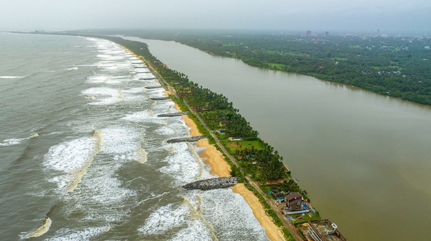 Aerial view of Mattu Beach featuring a narrow strip of land separating the sea from the backwaters with stone breakwaters and palm trees in Udupi Karnataka India.