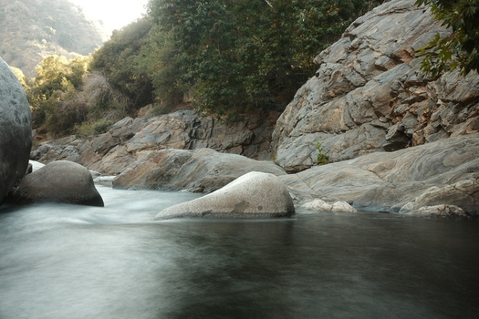 View of a flowing river surrounded by large granite boulders and lush green forest in Sequoia National Park Tulare County California United States. View of a flowing river surrounded by large granite boulders and lush green forest in Sequoia National Park Tulare County California United States.
