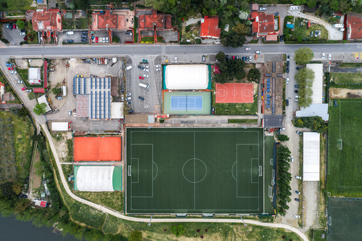 Aerial view of a sports complex featuring a green soccer pitch tennis courts and a basketball court surrounded by residential buildings in Leccio Toscana Italy. Aerial view of a sports complex featuring a green soccer pitch tennis courts and a basketball court surrounded by residential buildings in Leccio Toscana Italy.