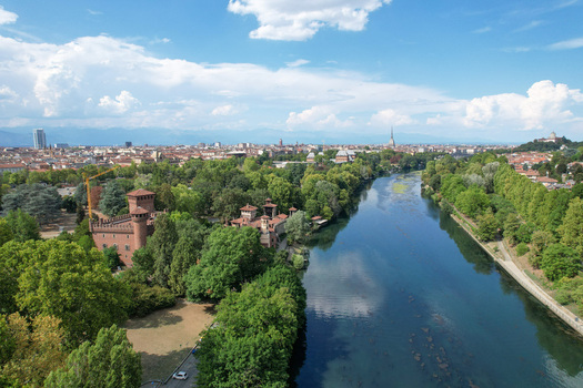 Aerial view of Borgo Medievale and the Po River flowing through Valentino Park with the city skyline and Mole Antonelliana in the distance Torino Piemonte Italy.
