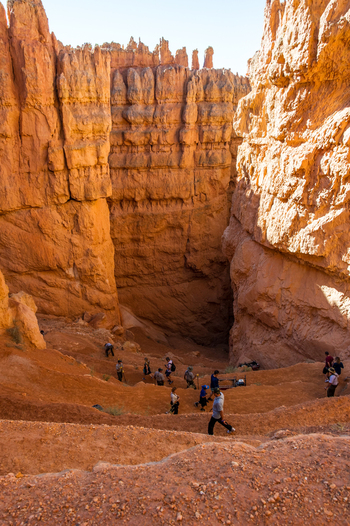 View of hikers walking along a trail surrounded by towering orange hoodoos and rock formations in Bryce Canyon National Park Utah United States.
