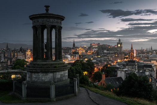 View of the Dugald Stewart Monument on Calton Hill overlooking the illuminated city skyline and Edinburgh Castle at twilight in Edinburgh Scotland United Kingdom. View of the Dugald Stewart Monument on Calton Hill overlooking the illuminated city skyline and Edinburgh Castle at twilight in Edinburgh Scotland United Kingdom.