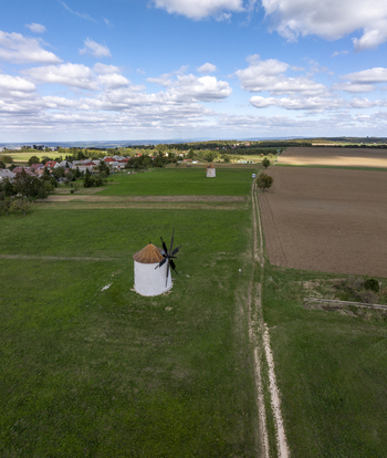 Aerial view of the historic Regi Szelmalom windmills set in a green field with a dirt path and agricultural land under a blue sky in Tes Hungary. Aerial view of the historic Regi Szelmalom windmills set in a green field with a dirt path and agricultural land under a blue sky in Tes Hungary.