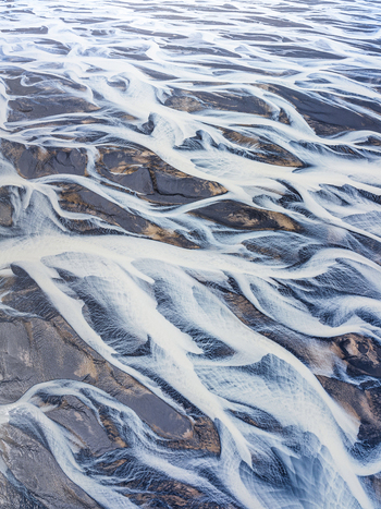 Aerial view of a braided river system with glacial meltwater channels flowing through dark volcanic sediment in Iceland. Aerial view of a braided river system with glacial meltwater channels flowing through dark volcanic sediment in Iceland.