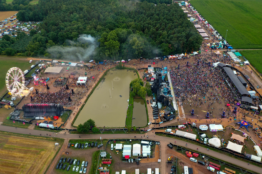 Herzogenaurach Germany 26 July 2025 Aerial view of Open Beatz Festival with large crowds of people gathered around stages and a Ferris wheel near a lush forest.