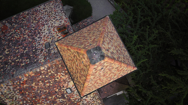 Aerial view of the distinctive multi colored tiled roof and square tower of a historic building surrounded by green trees in Luins Vaud Switzerland. Aerial view of the distinctive multi colored tiled roof and square tower of a historic building surrounded by green trees in Luins Vaud Switzerland.