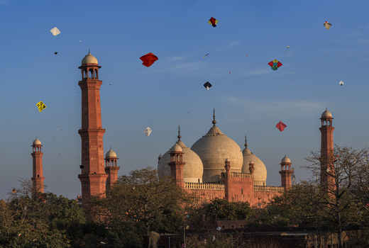 View of the historic Badshahi Mosque with numerous colorful kites flying in the blue sky during the Basant festival in Lahore Punjab Pakistan.