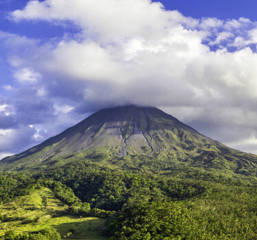 Aerial view of Arenal Volcano with a cloud cap above its peak and lush tropical forest covering the slopes in Costa Rica.